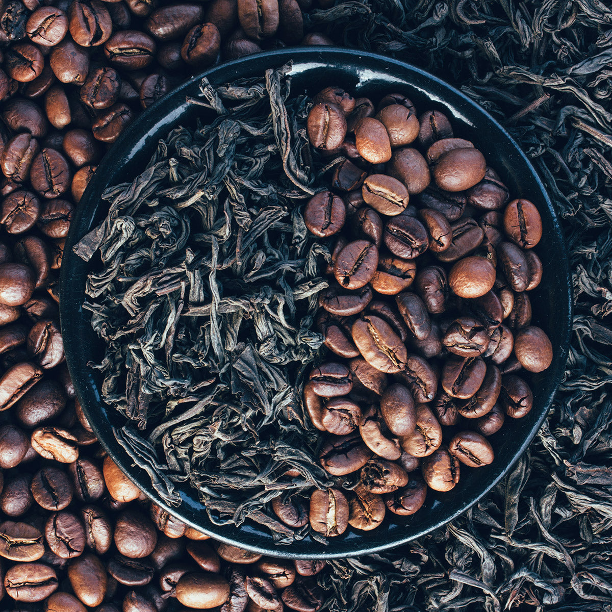 Tea leaves and coffee beans side by side in a bowl